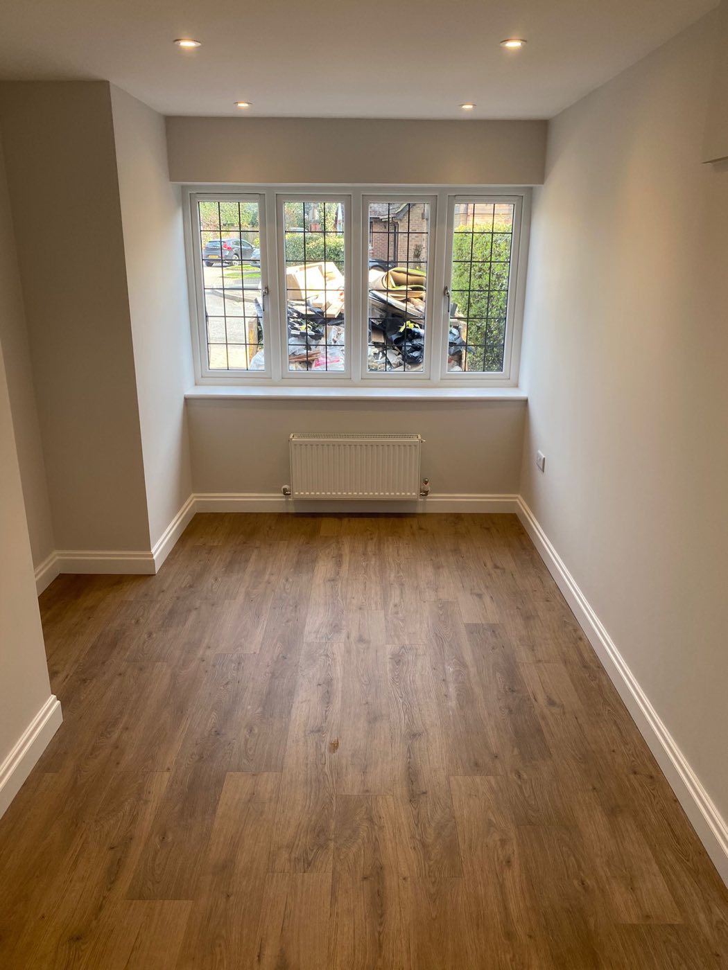 The finished room with wood-effect flooring, a radiator and recessed downlights